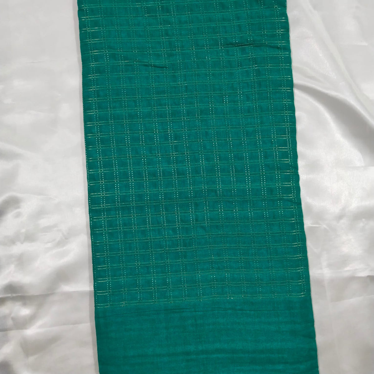 A teal green woven fabric runner with a subtle grid pattern and a solid border at the bottom, laid flat on a white satin background.