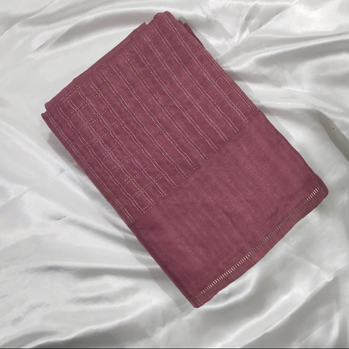 A folded dusty rose pink striped fabric, likely a scarf, shawl, or throw, displayed on a draped white satin background.